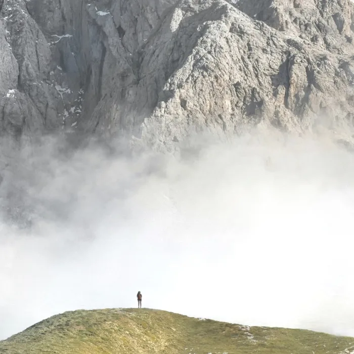 Lone hiker on a ridge, facing a mountain wall in the mist