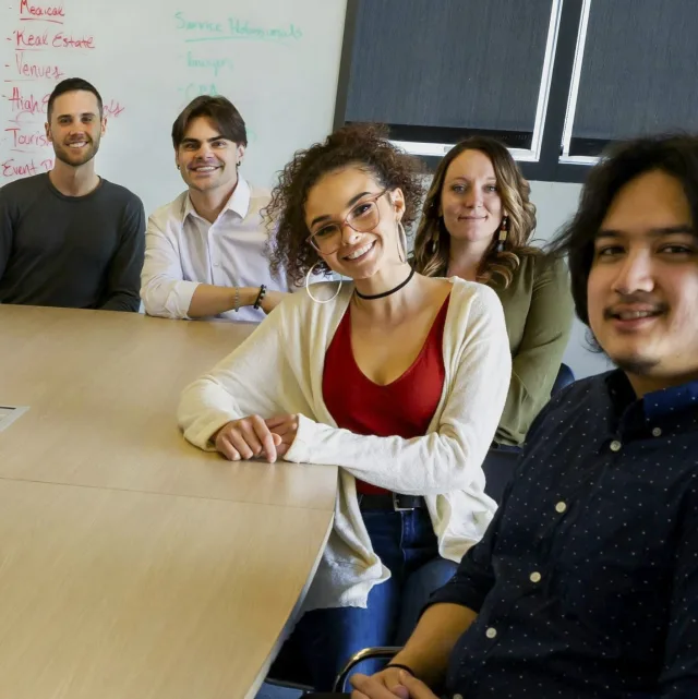 Five smiling colleagues gathered around a meeting table in a company conference room