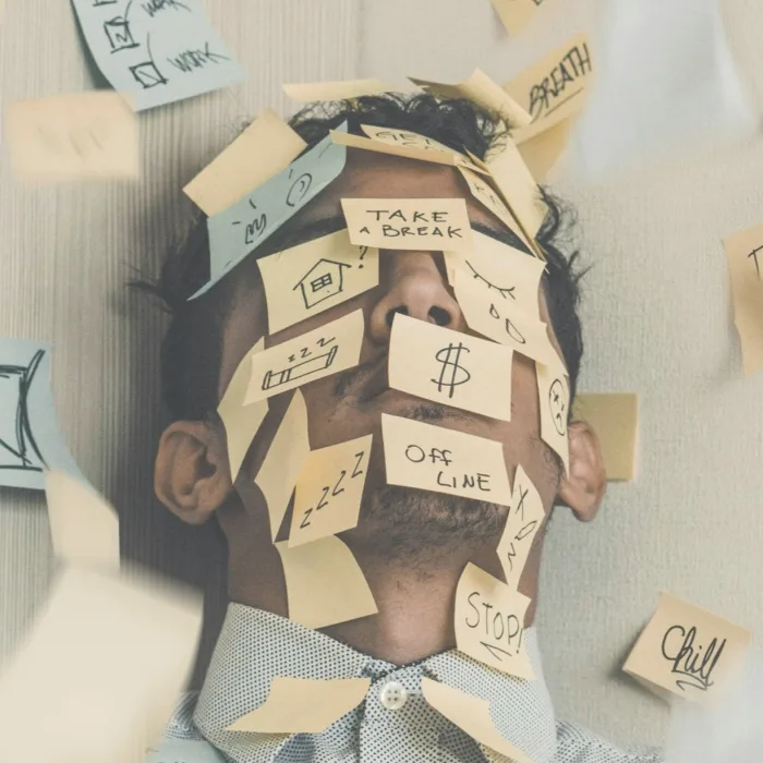 Man at work buried under sticky notes, illustrating workplace stress