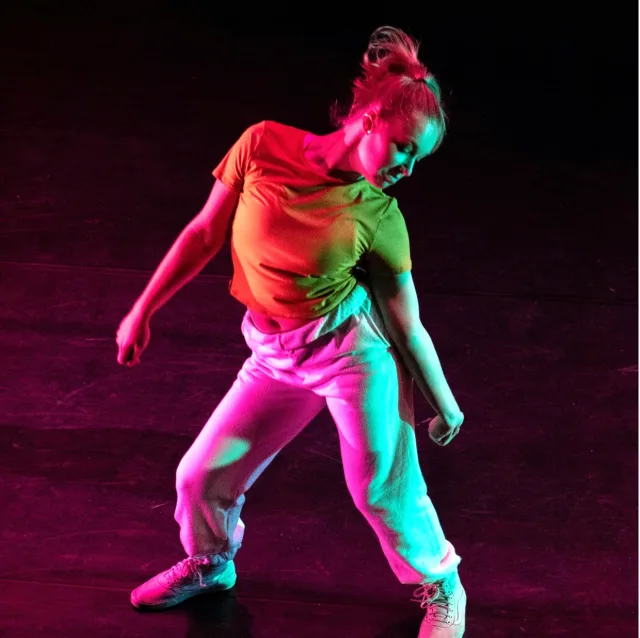 Danseuse en pleine performance, éclairée de lumières colorées sur scène