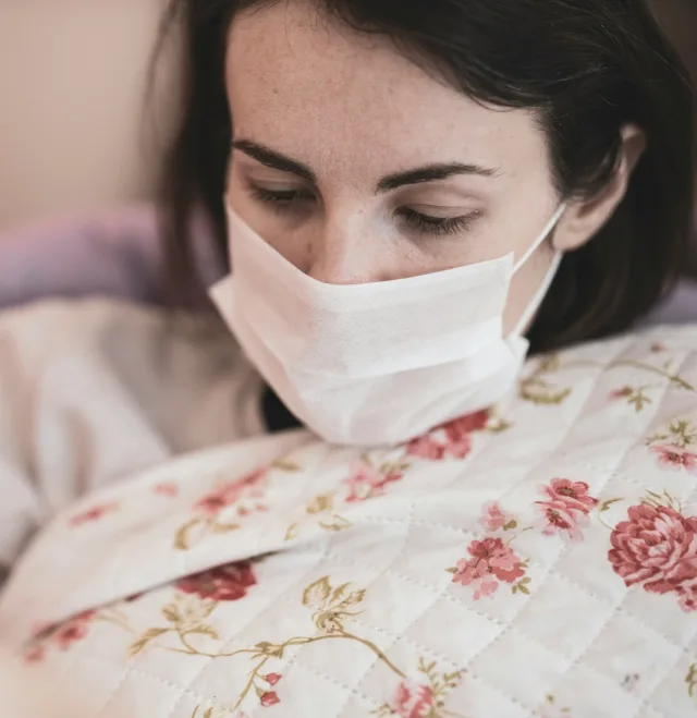 Woman lying in bed wearing a face mask, eyes lowered